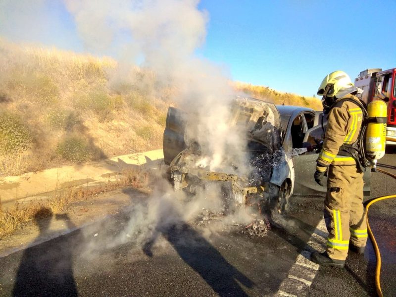 Un bombero apaga el fuego del Opel Corsa en el arcén de la SE-40.